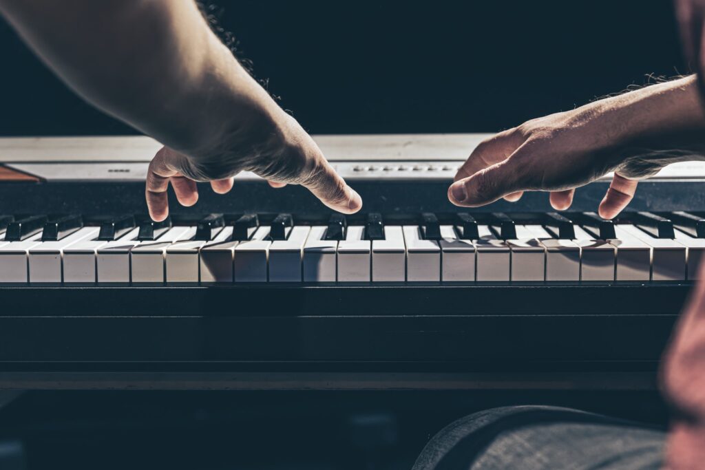 Male hands play the keys of the piano in the dark close-up, the concept of musical creativity.